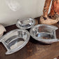 Three silver metal bowls on a wooden surface with a decorative elephant figurine in the background.