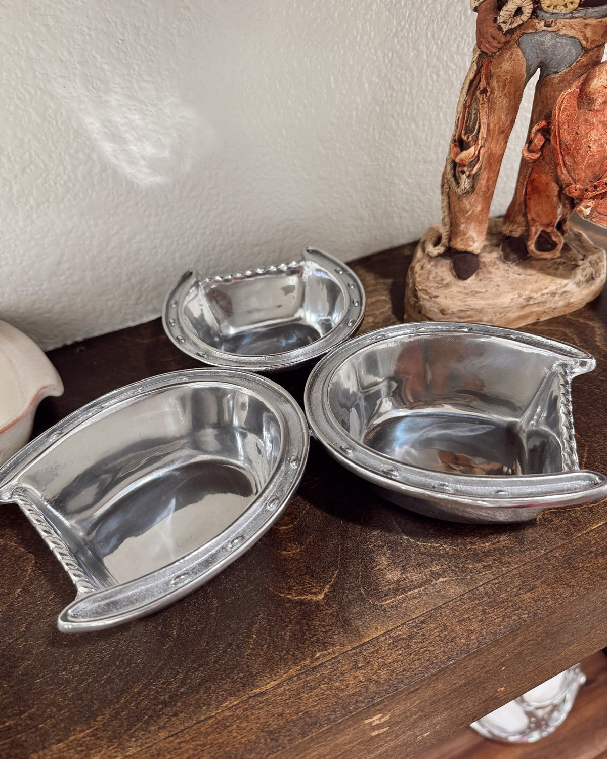 Three silver metal bowls on a wooden surface with a decorative elephant figurine in the background.