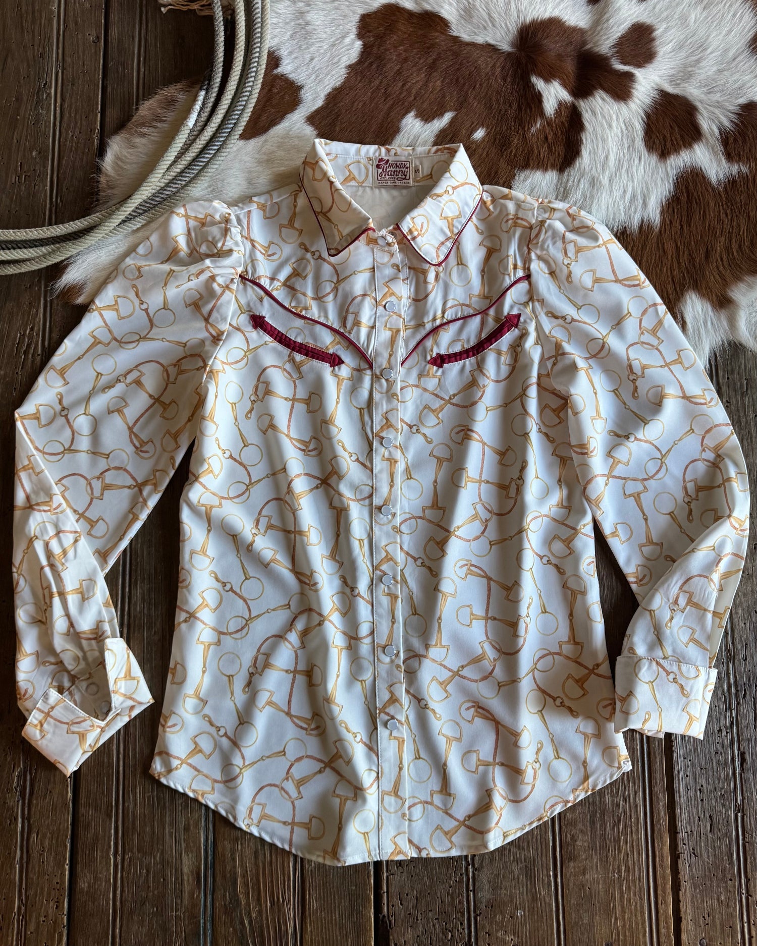 White long-sleeve shirt with red embroidery on a wooden surface with cowhide rug