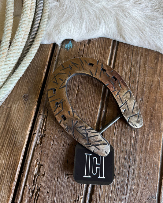 Decorative horseshoe on a wooden surface with a cowhide and rope in the background