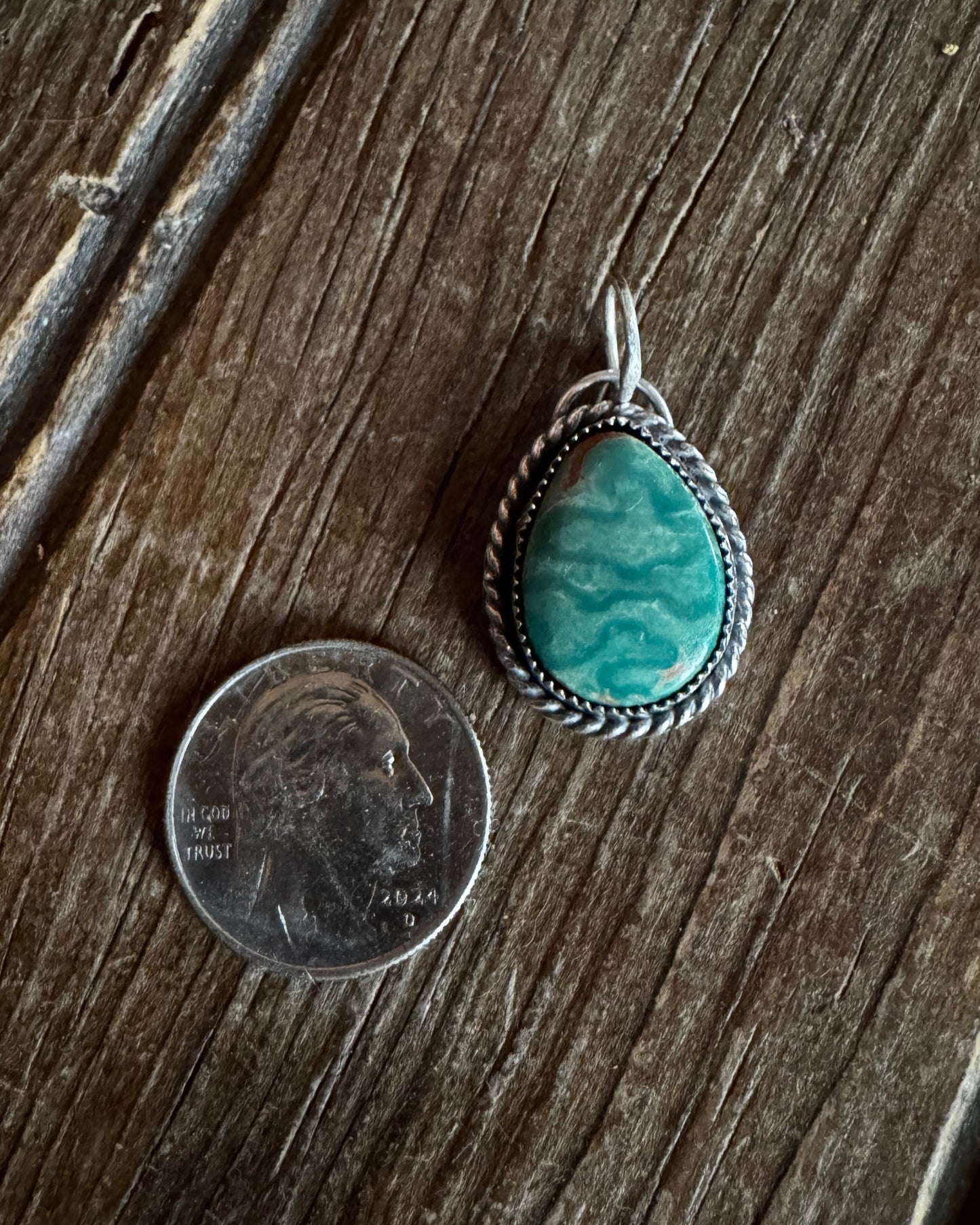 Turquoise stone pendant on a wooden surface with a coin for scale