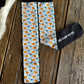 A pair of crew socks with a light blue background and an all-over pattern of orange dogs and teal birds, laid flat on a rustic wooden surface next to a black sock tag that reads 'RED BARN SOCKS'.