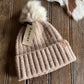 Beige knit beanie with pom-pom and Ariat tag on a wooden surface