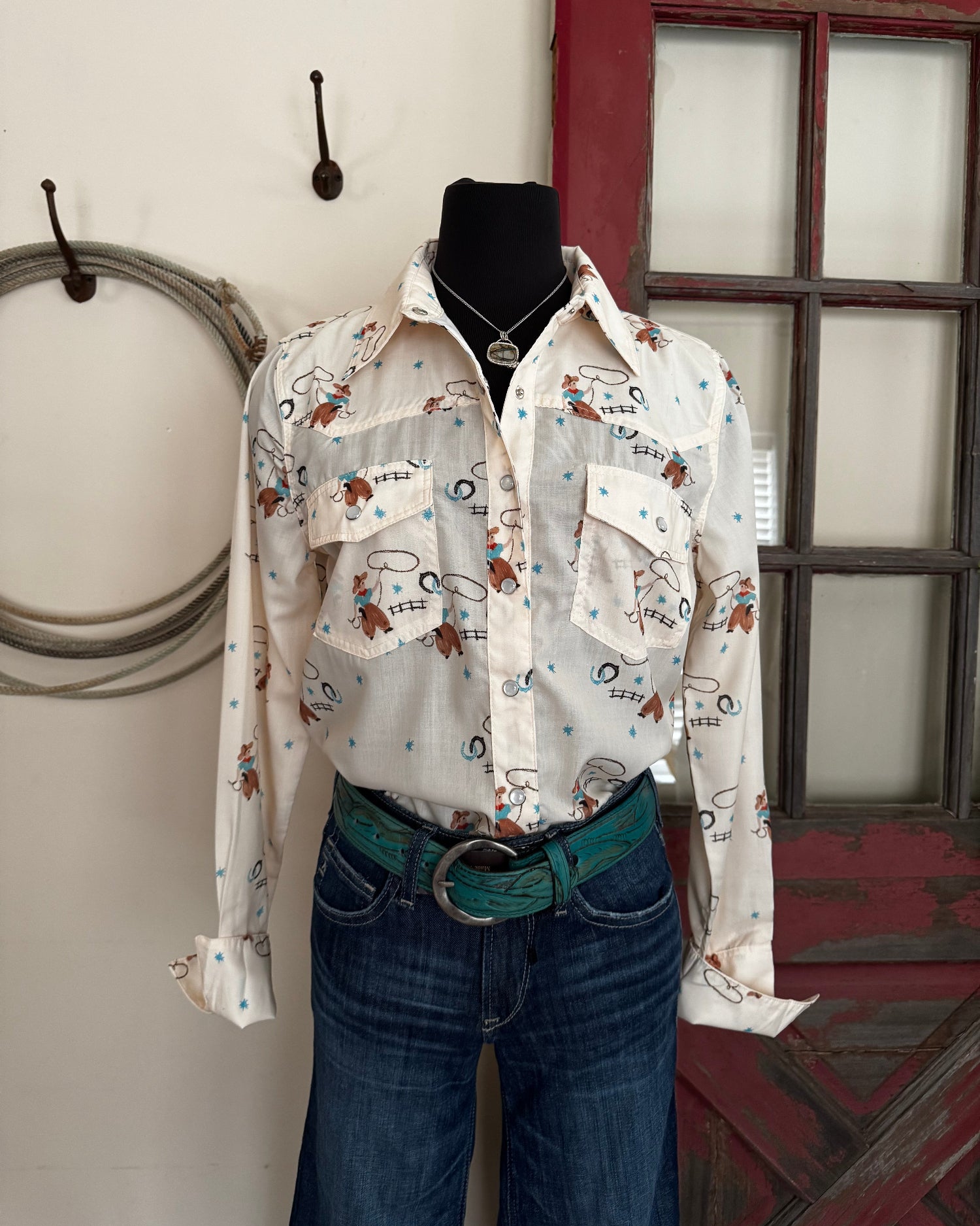 Mannequin wearing a patterned shirt and jeans standing in front of a window.