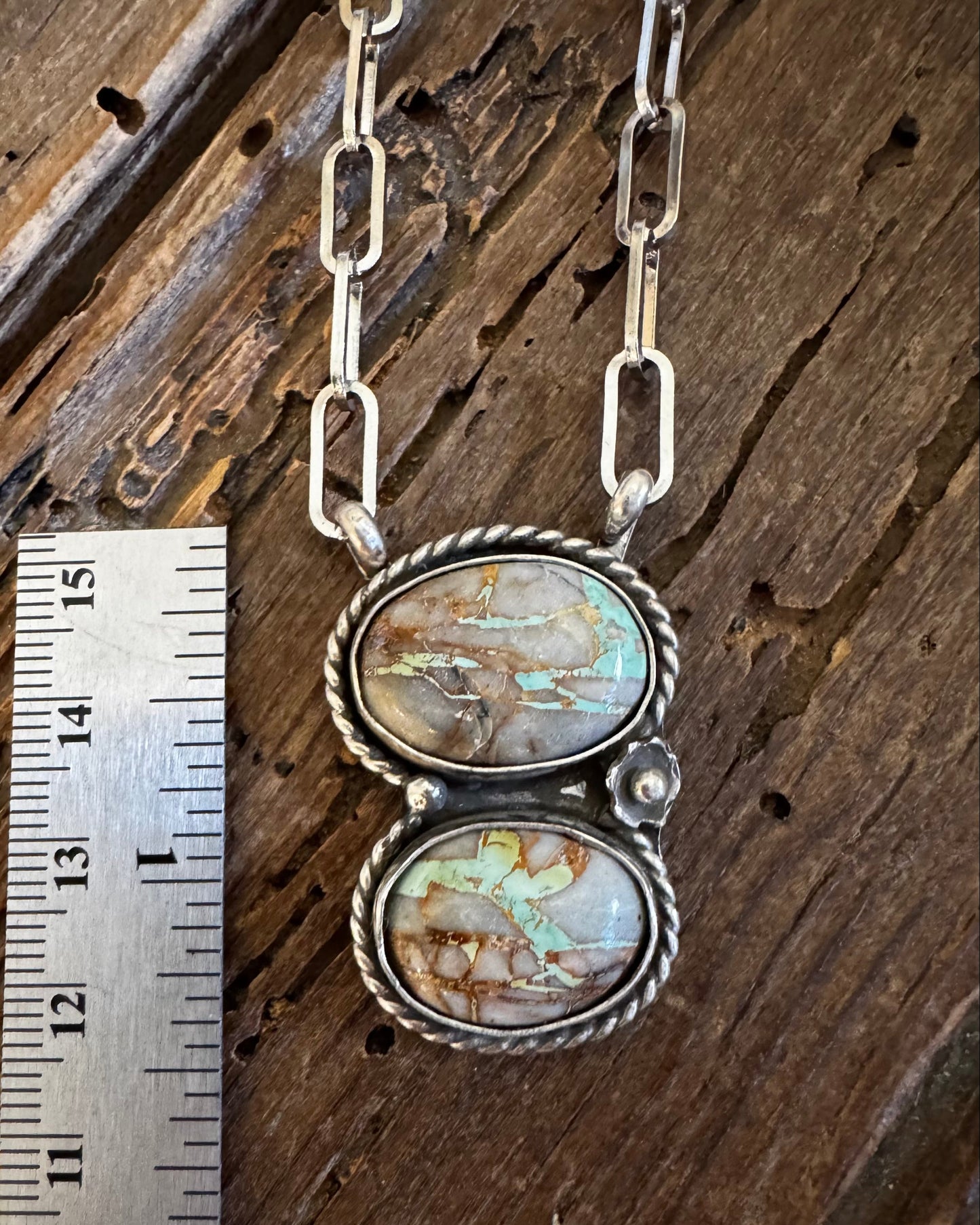 Necklace with a double pendant on a wooden surface next to a ruler for scale.