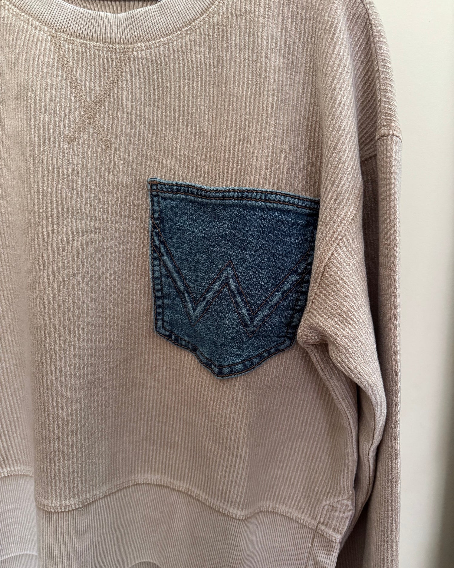 Close-up of a beige corduroy garment with a blue denim pocket detail.