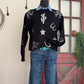 Black sweater with white designs on a mannequin against a rustic background