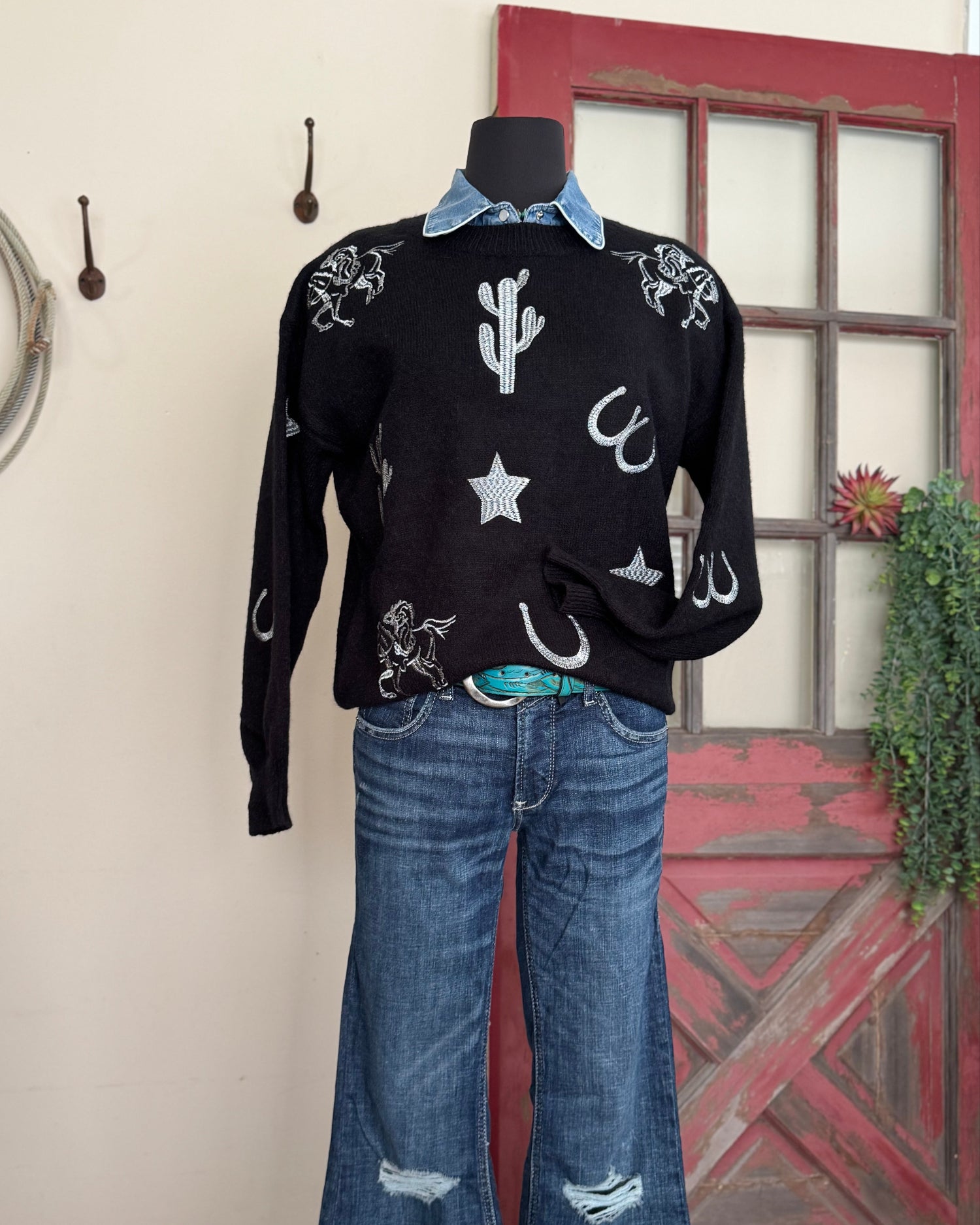 Black sweater with white designs on a mannequin against a rustic background