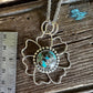 Silver pendant with turquoise stone on a wooden surface next to a ruler