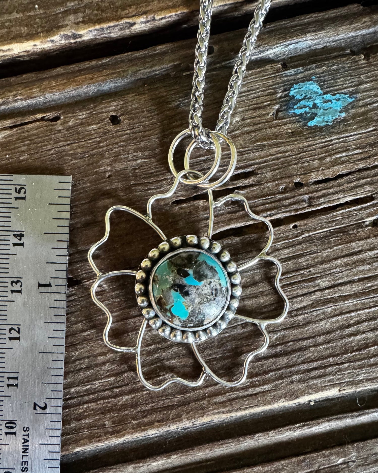 Silver pendant with turquoise stone on a wooden surface next to a ruler
