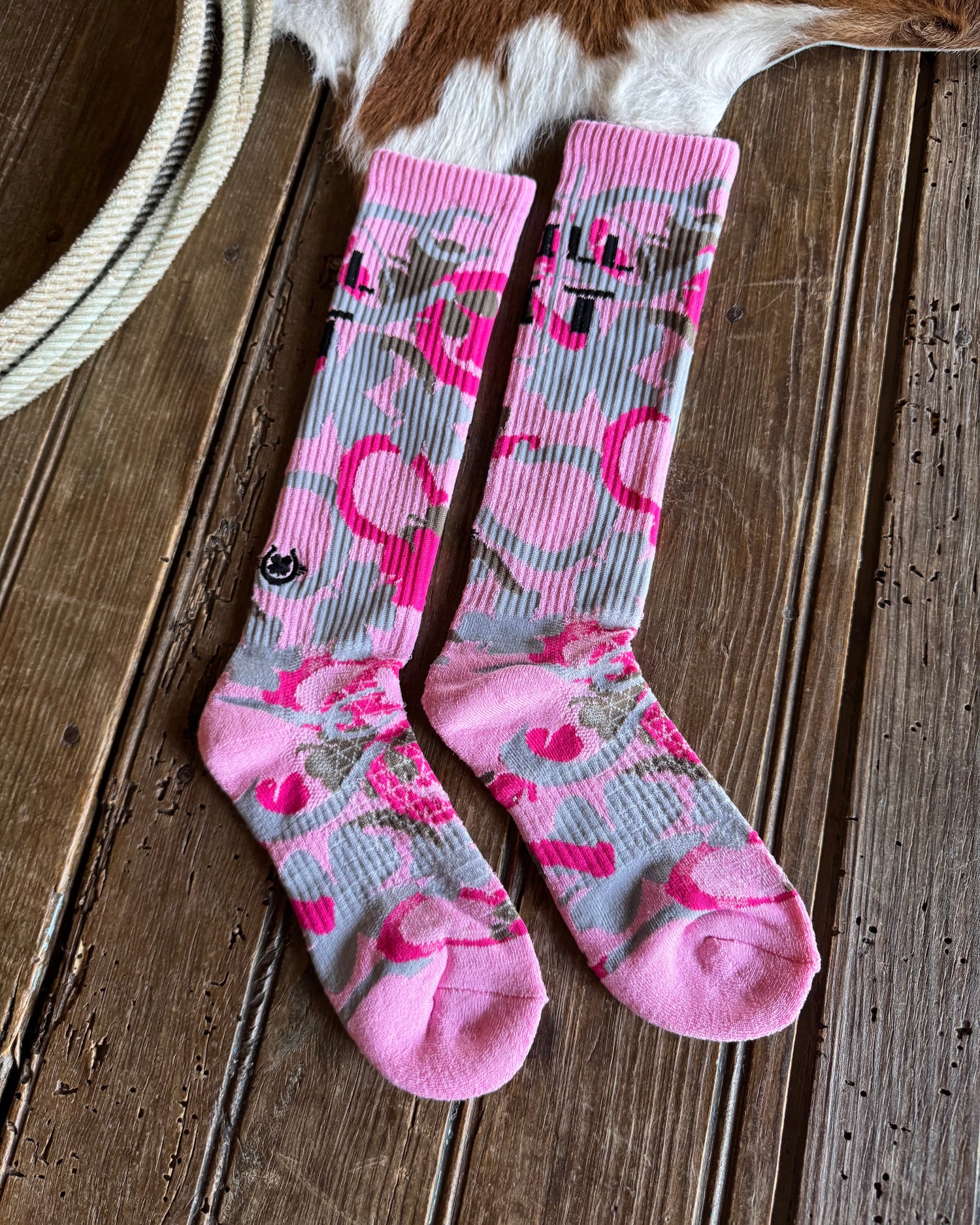 Pair of pink and gray patterned socks on a wooden surface with a cowhide rug.