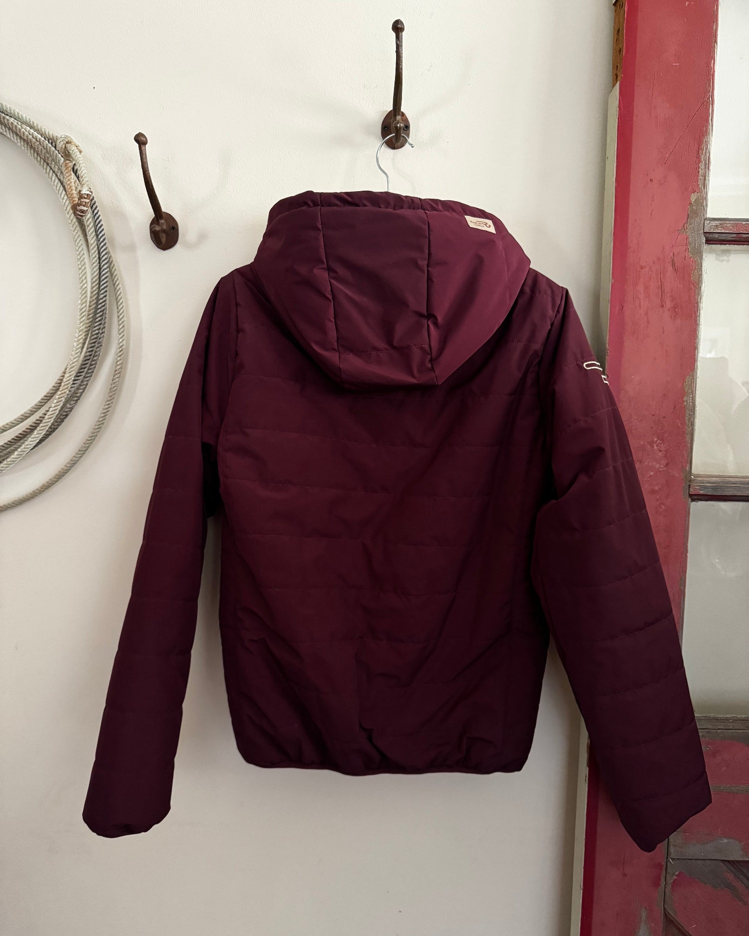 Maroon jacket on a white surface with a red frame in the background