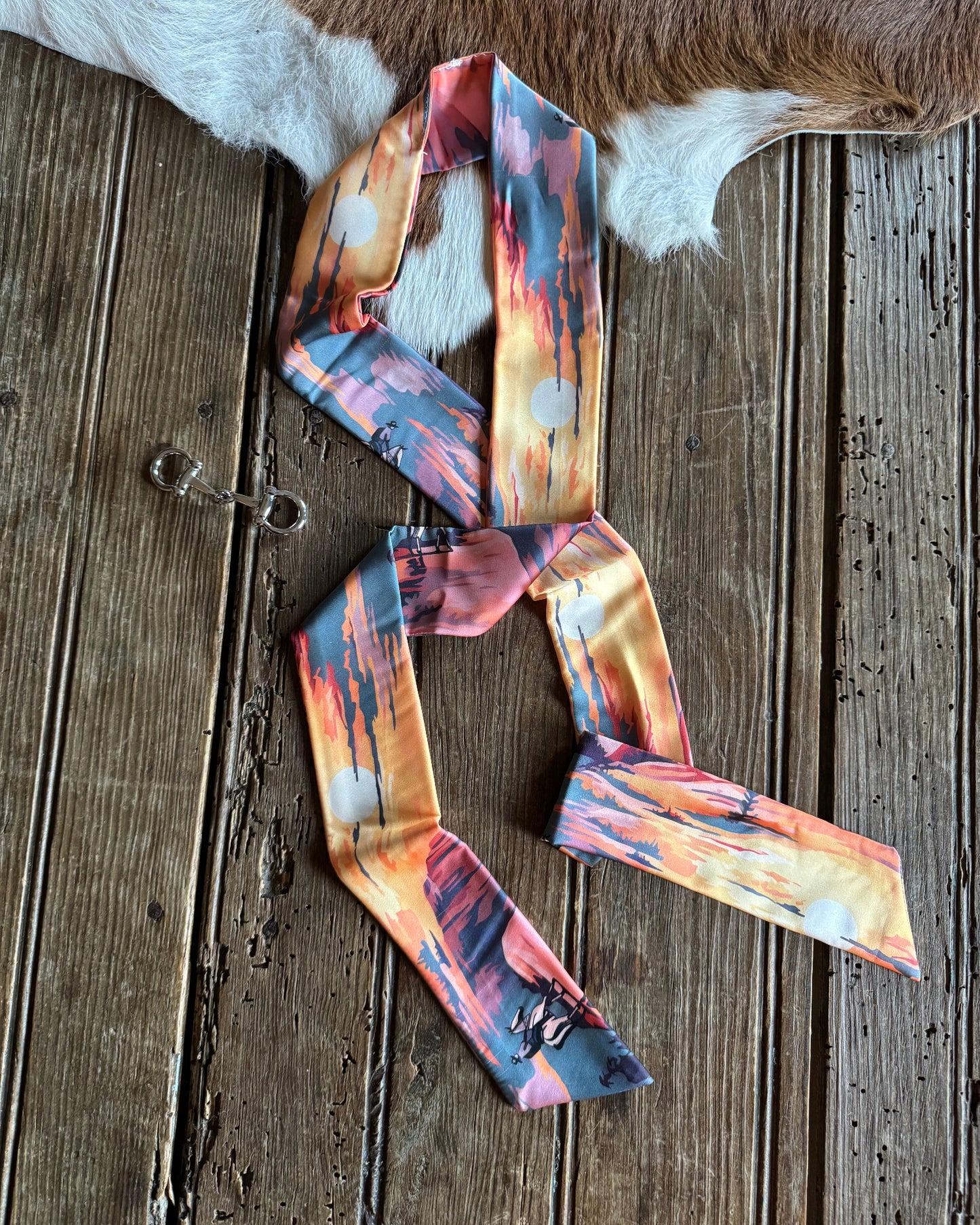 Colorful patterned ribbon scarf on a wooden surface with a cowhide rug.