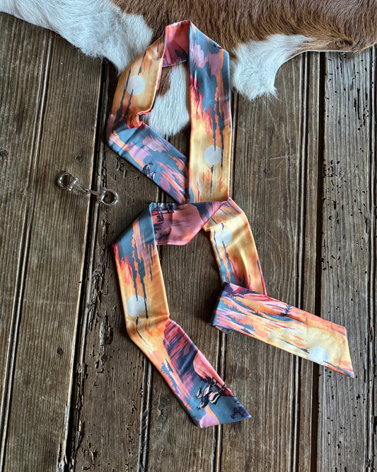 Colorful patterned ribbon scarf on a wooden surface with a cowhide rug.