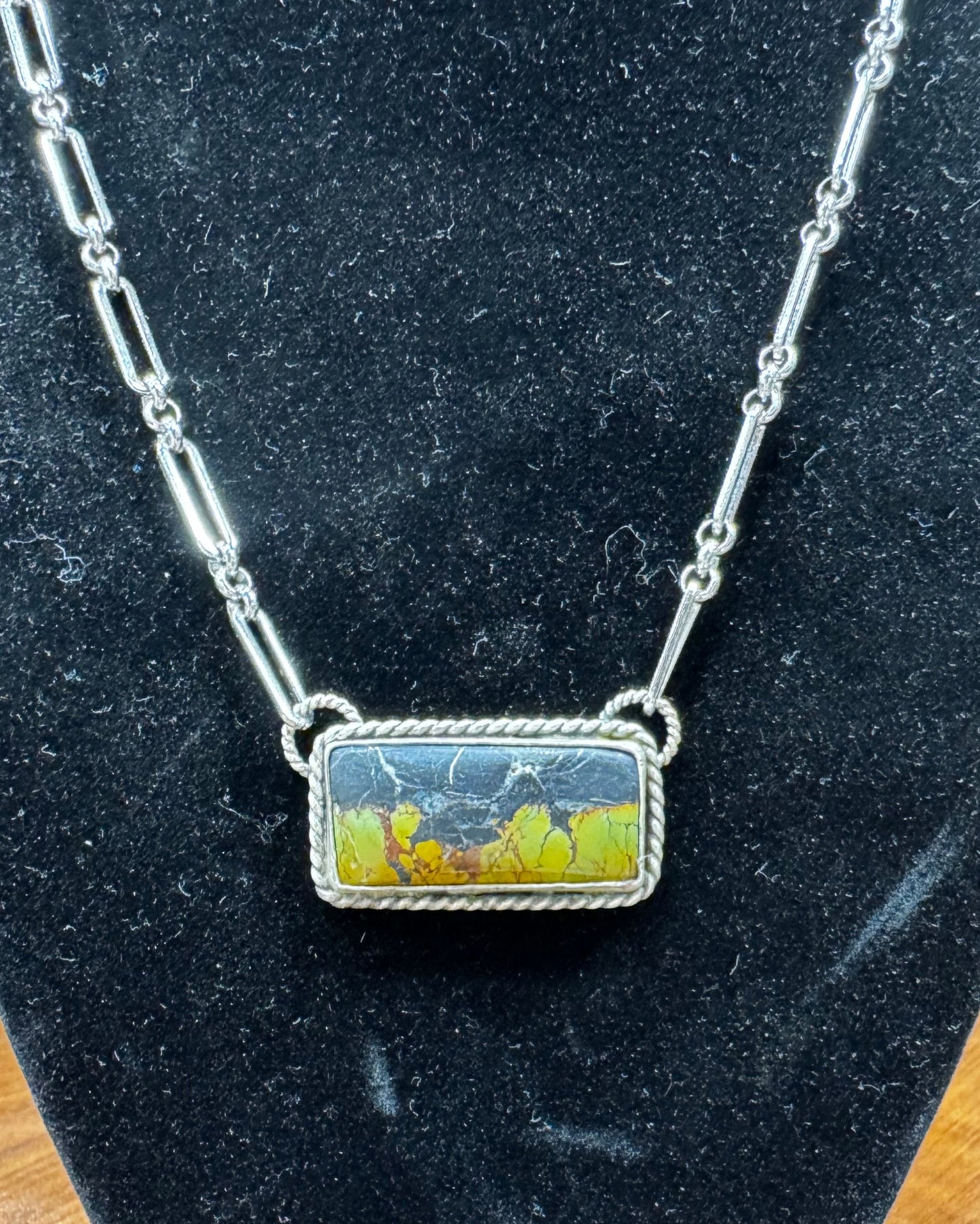 Necklace with a rectangular pendant on a black velvet stand.