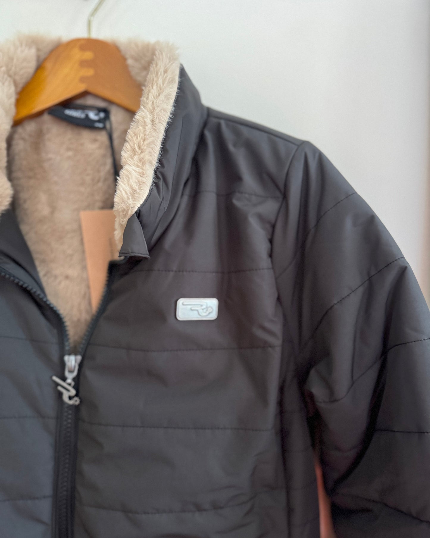 Dark gray jacket with beige fur lining on a hanger against a white wall