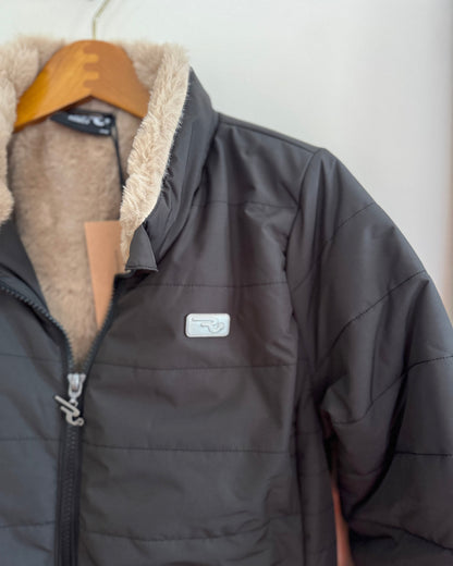 Dark gray jacket with beige fur lining on a hanger against a white wall