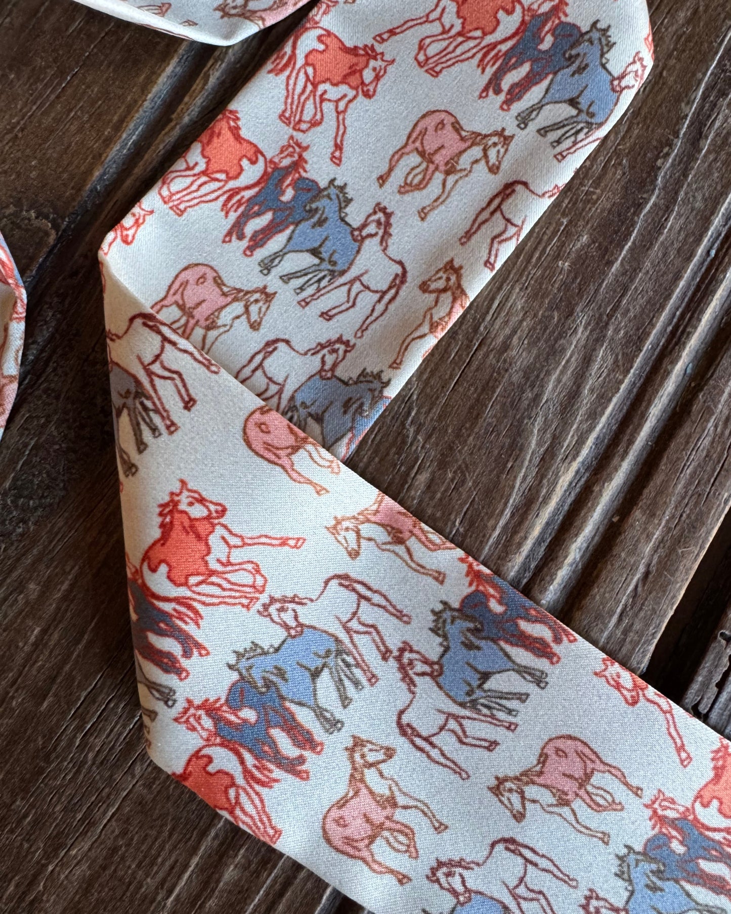 close up of ribbon scarf with horses on a rustic wood background
