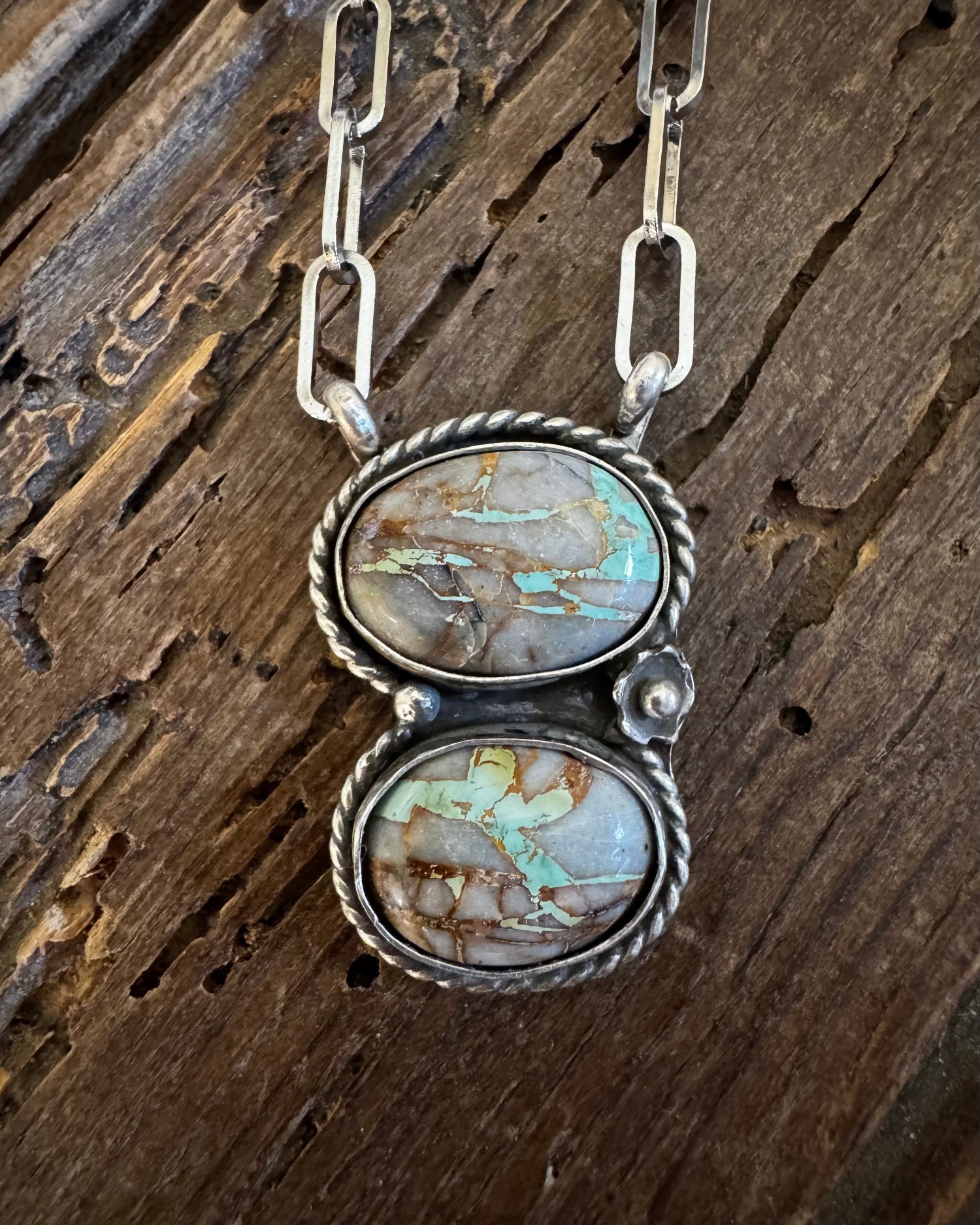 Silver necklace with two turquoise stone pendants on a wooden surface
