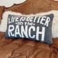 Decorative pillow with 'Life is better on the ranch' text on a brown leather couch.