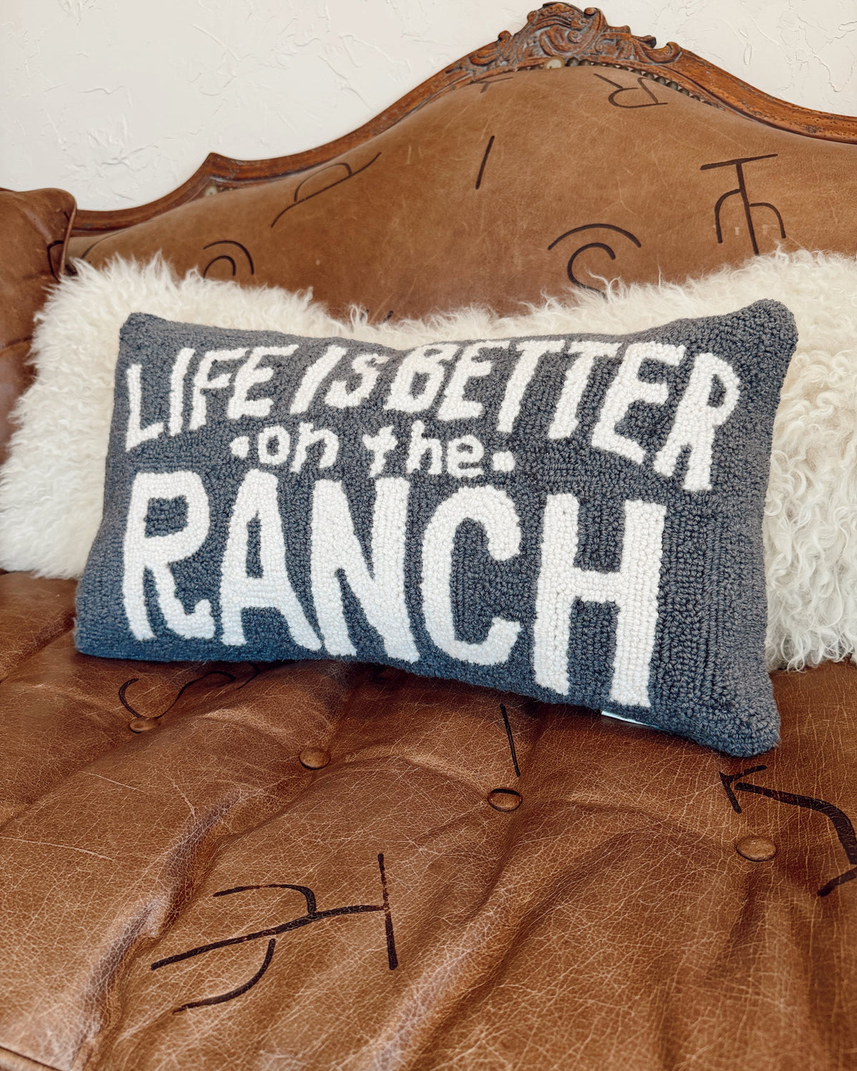 Decorative pillow with 'Life is better on the ranch' text on a brown leather couch.