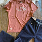 Pink t-shirt with 'Ranch Girls' logo and dark blue jeans on a wooden surface.