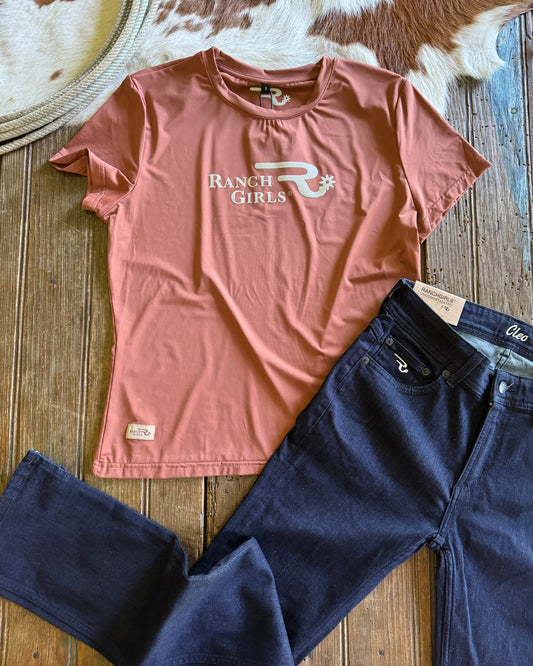 Pink t-shirt with 'Ranch Girls' logo and dark blue jeans on a wooden surface.