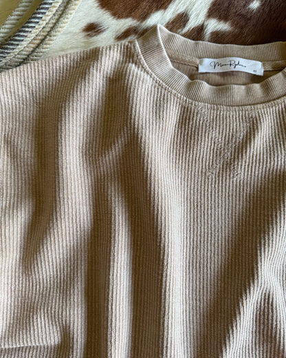Beige ribbed tank top with a brand label on a patterned surface