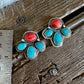 A pair of silver-toned paw-shaped earrings with turquoise and coral stone inlays, displayed on a rustic wooden surface next to a metal ruler for scale.