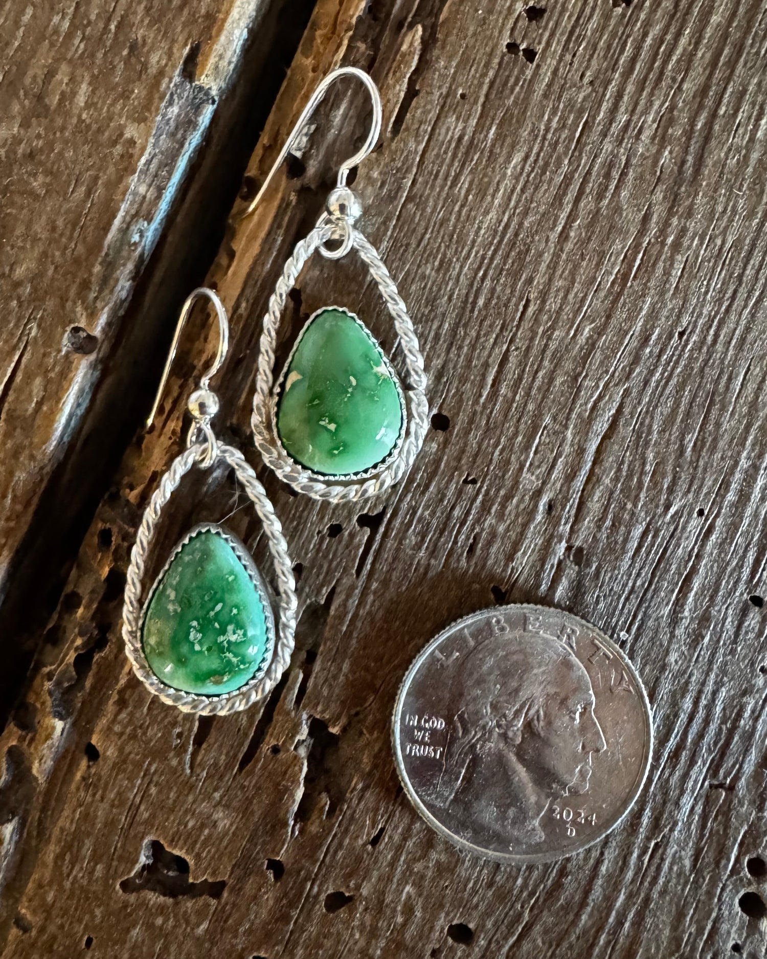 Green teardrop earrings with silver wire wrapping on a wooden surface next to a penny.