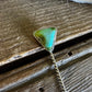 Turquoise triangle pendant on a chain against a wooden background