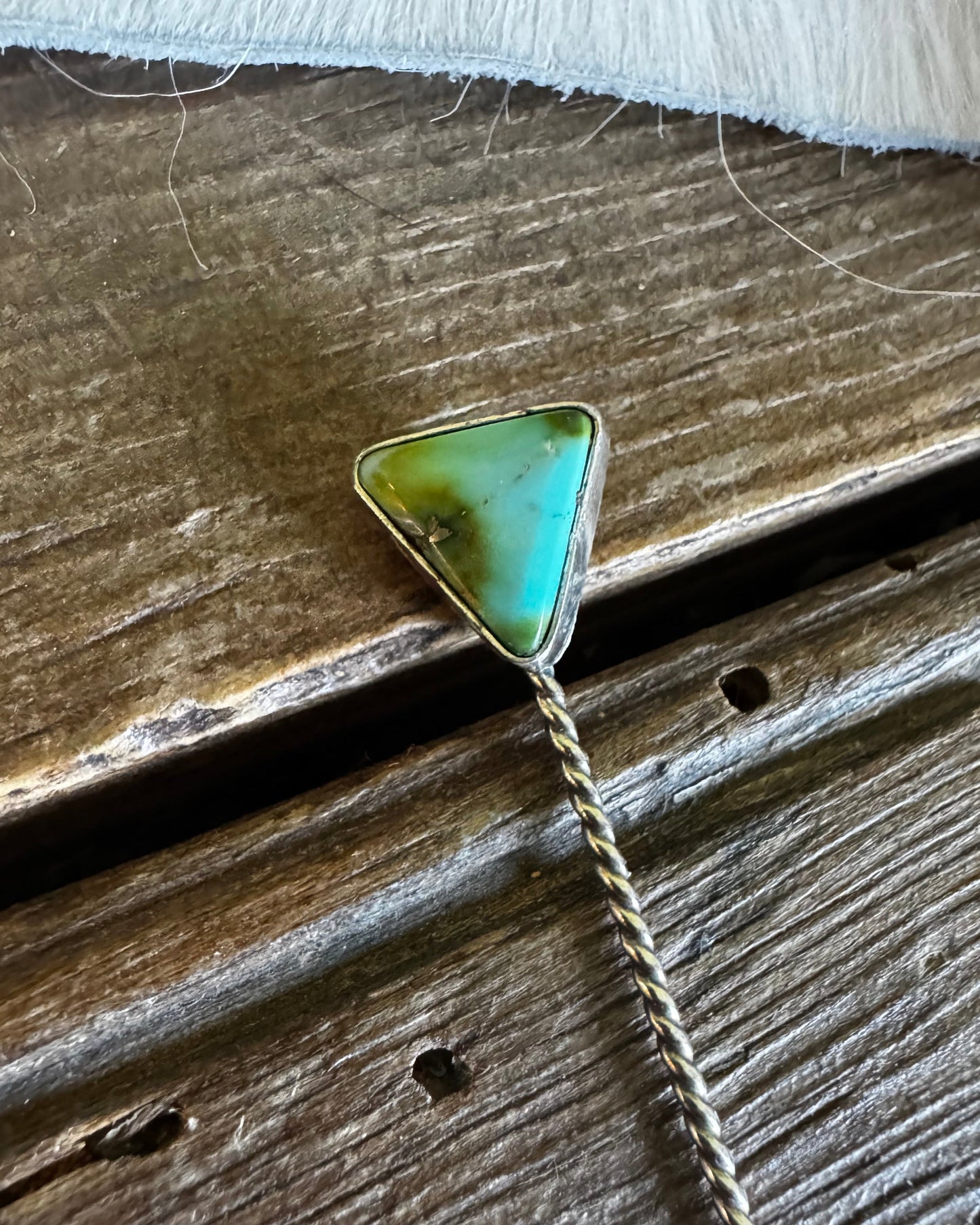 Turquoise triangle pendant on a chain against a wooden background