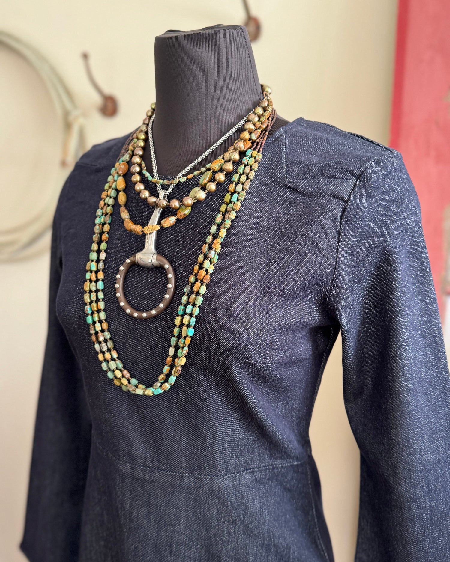 Mannequin wearing a denim dress with layered necklaces on a neutral background