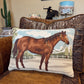 A rectangular woven throw pillow featuring a brown horse illustration, resting on a brown leather and embossed leather armchair in a living room setting.