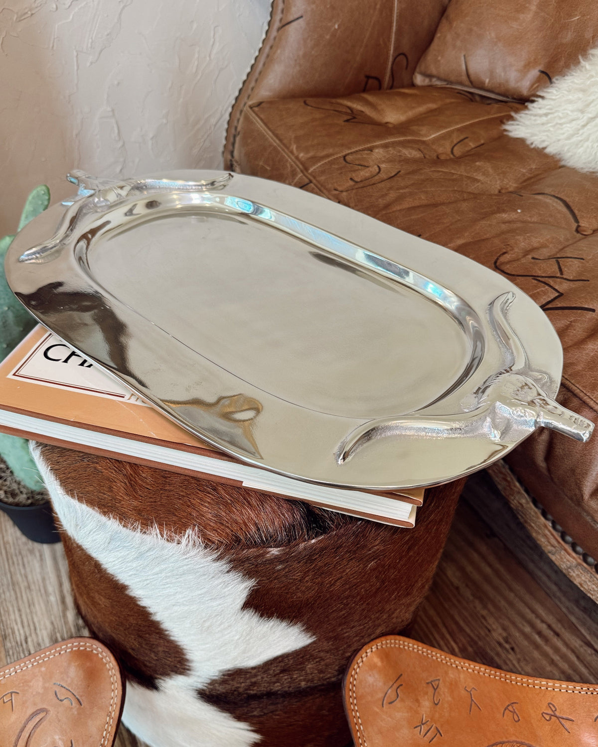 Silver tray on a wooden surface with a brown leather chair and cowhide rug in the background