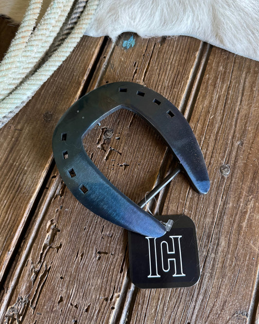 Horseshoe with a brand tag on a wooden surface next to a cowhide rug.