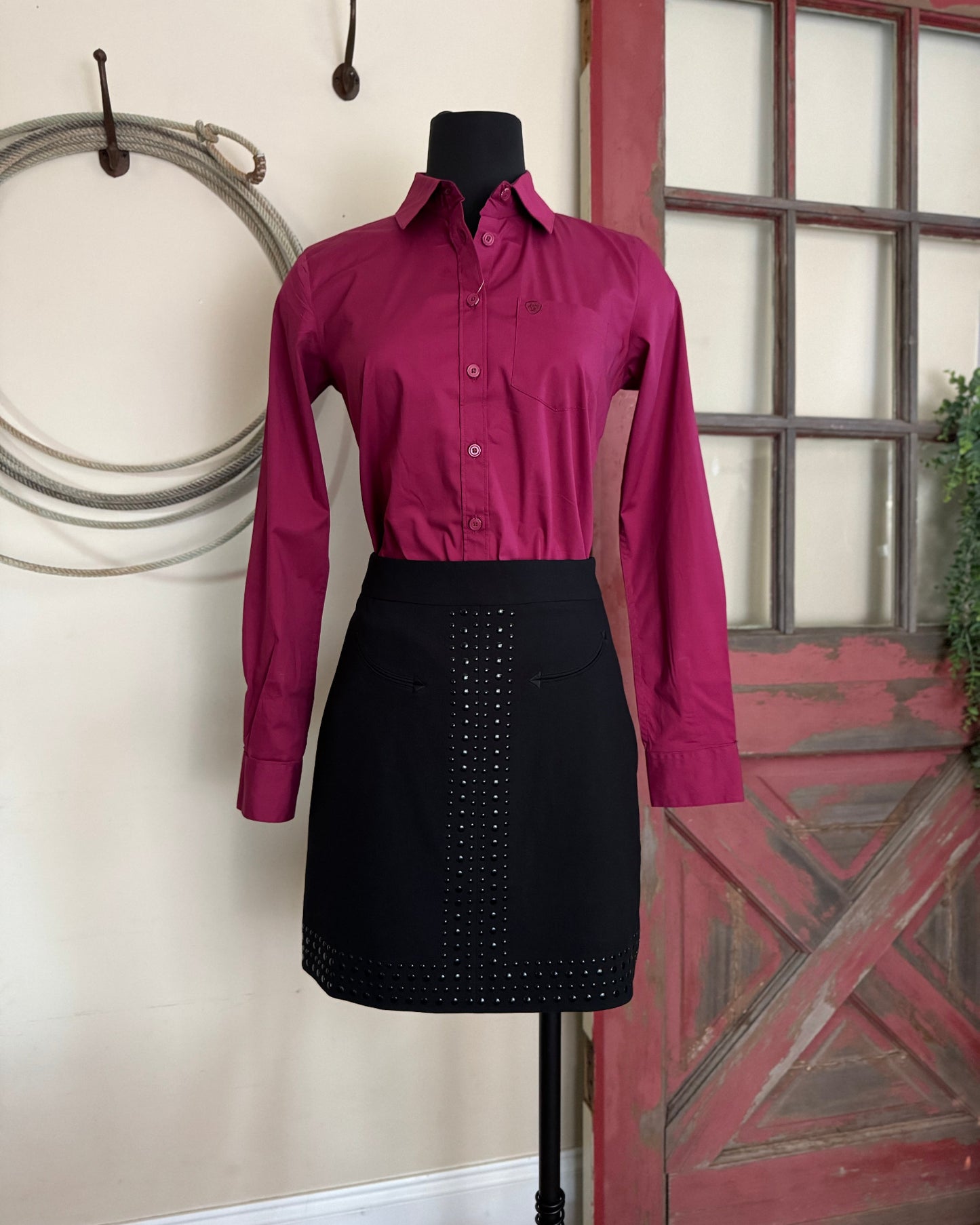 Mannequin wearing a maroon shirt and black skirt against a rustic background with a red door.