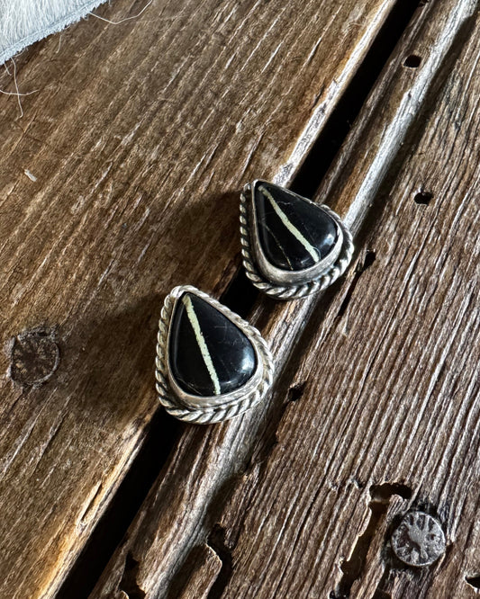 Pair of silver earrings with black stones on a wooden surface