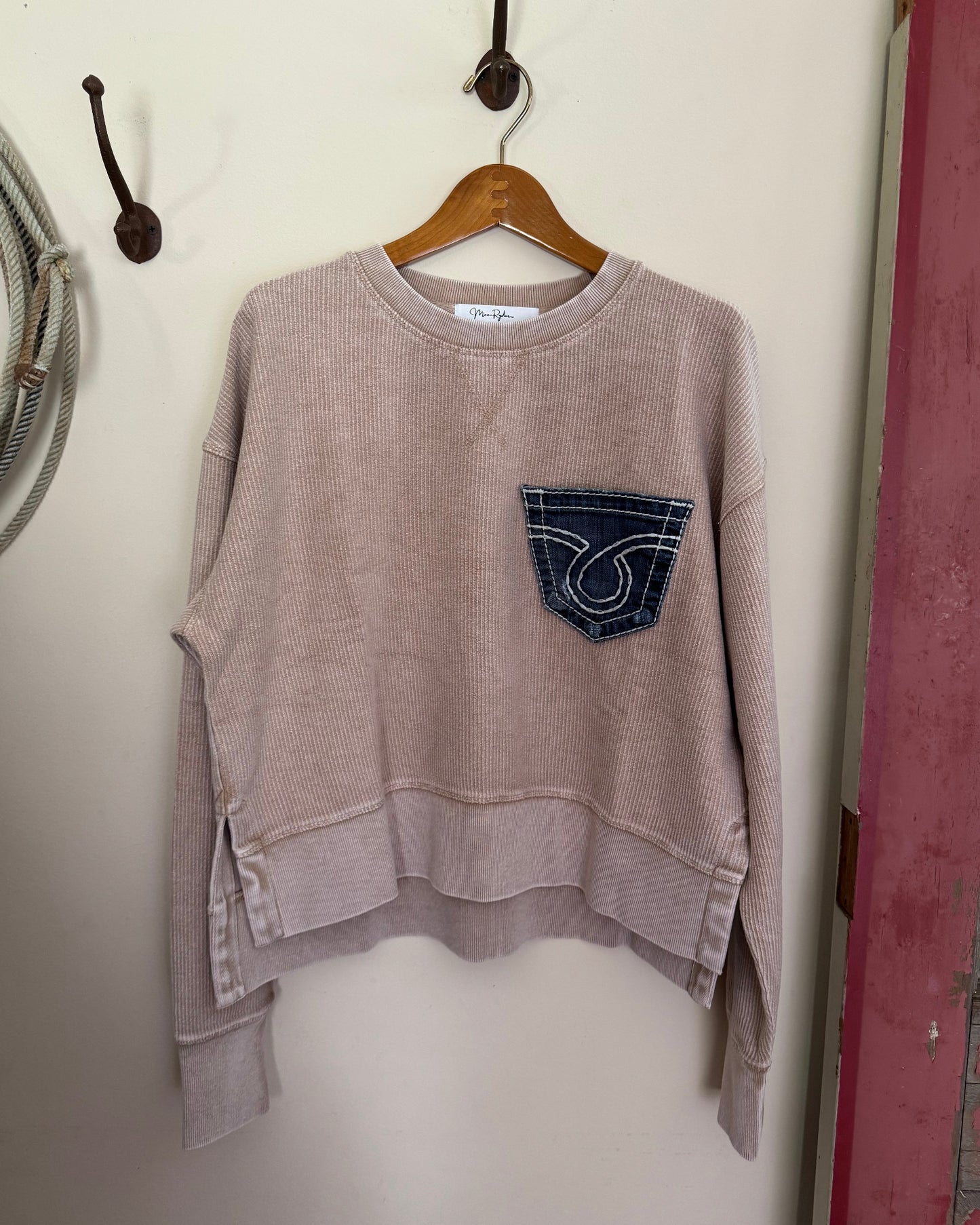 Brown sweatshirt with a logo on a hanger against a white wall.