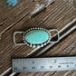 Turquoise stone pendant with silver chain on a wooden surface with a ruler for scale.