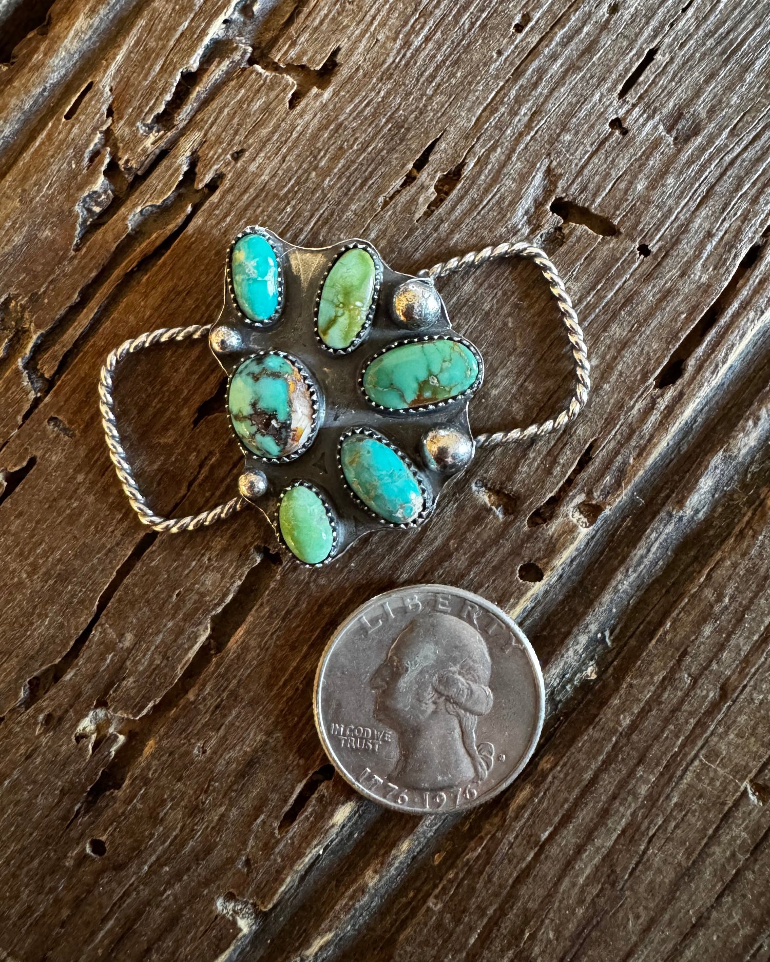 Turquoise pendant with gold accents on a wooden surface next to a penny for scale.