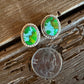 Pair of earrings with green stones next to a penny on wooden surface