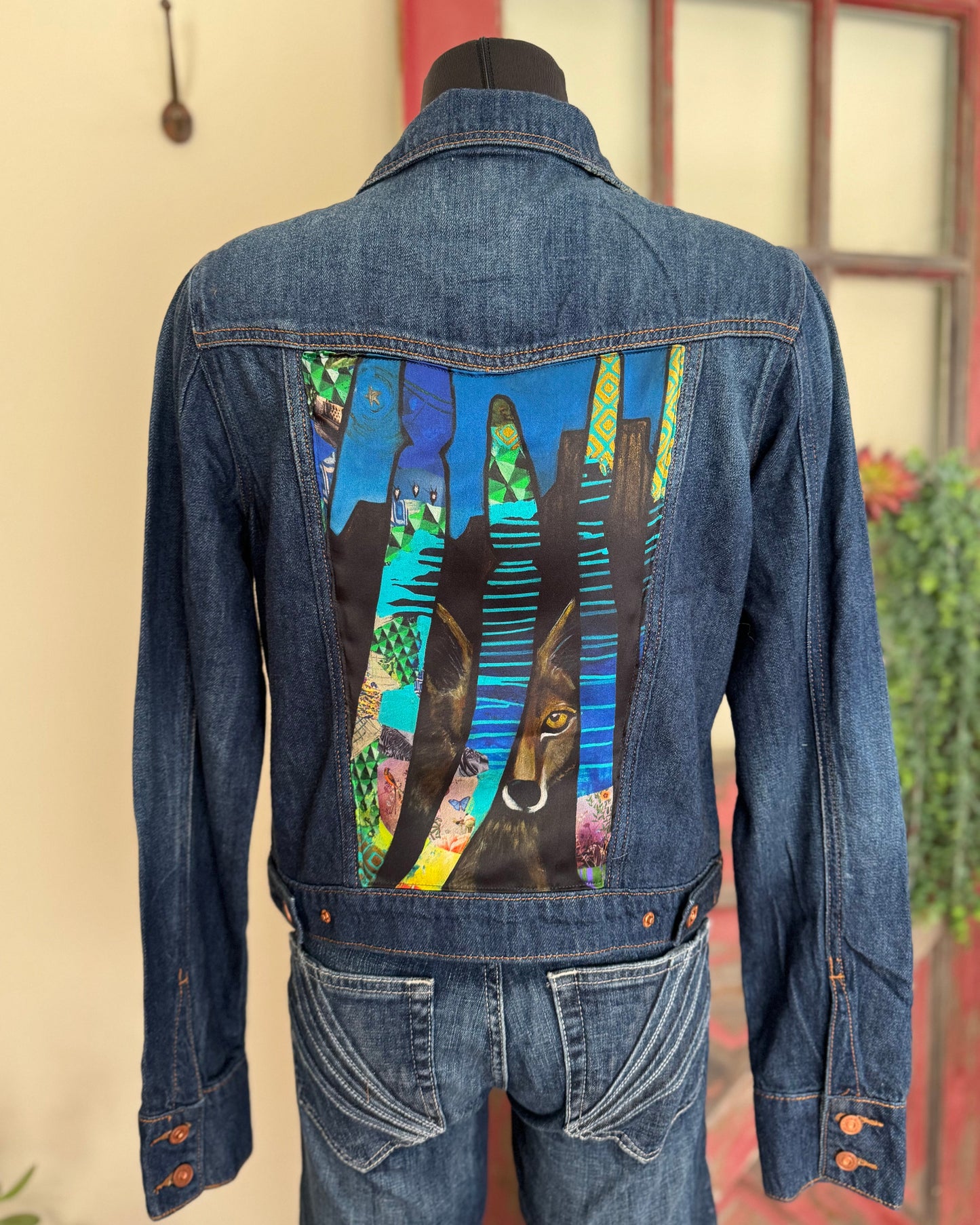 Blue denim jacket with colorful coyote design on the back, displayed on a mannequin against a neutral background.
