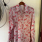 A long-sleeve button-up shirt with an allover red horse and rider pattern, hanging on a wooden hanger against a white wall.