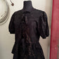Black patterned blouse on a mannequin against a neutral wall with a red door.