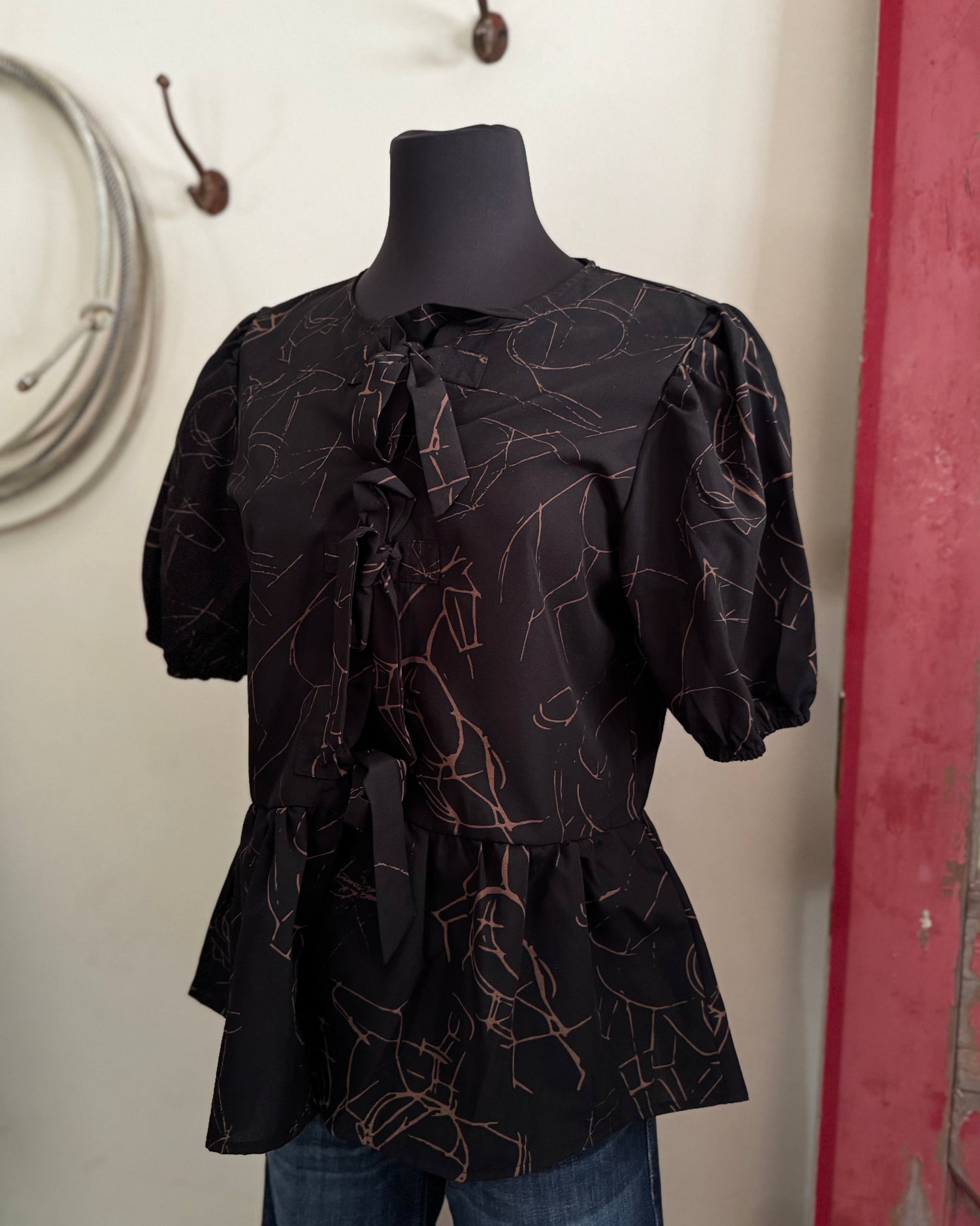 Black patterned blouse on a mannequin against a neutral wall with a red door.