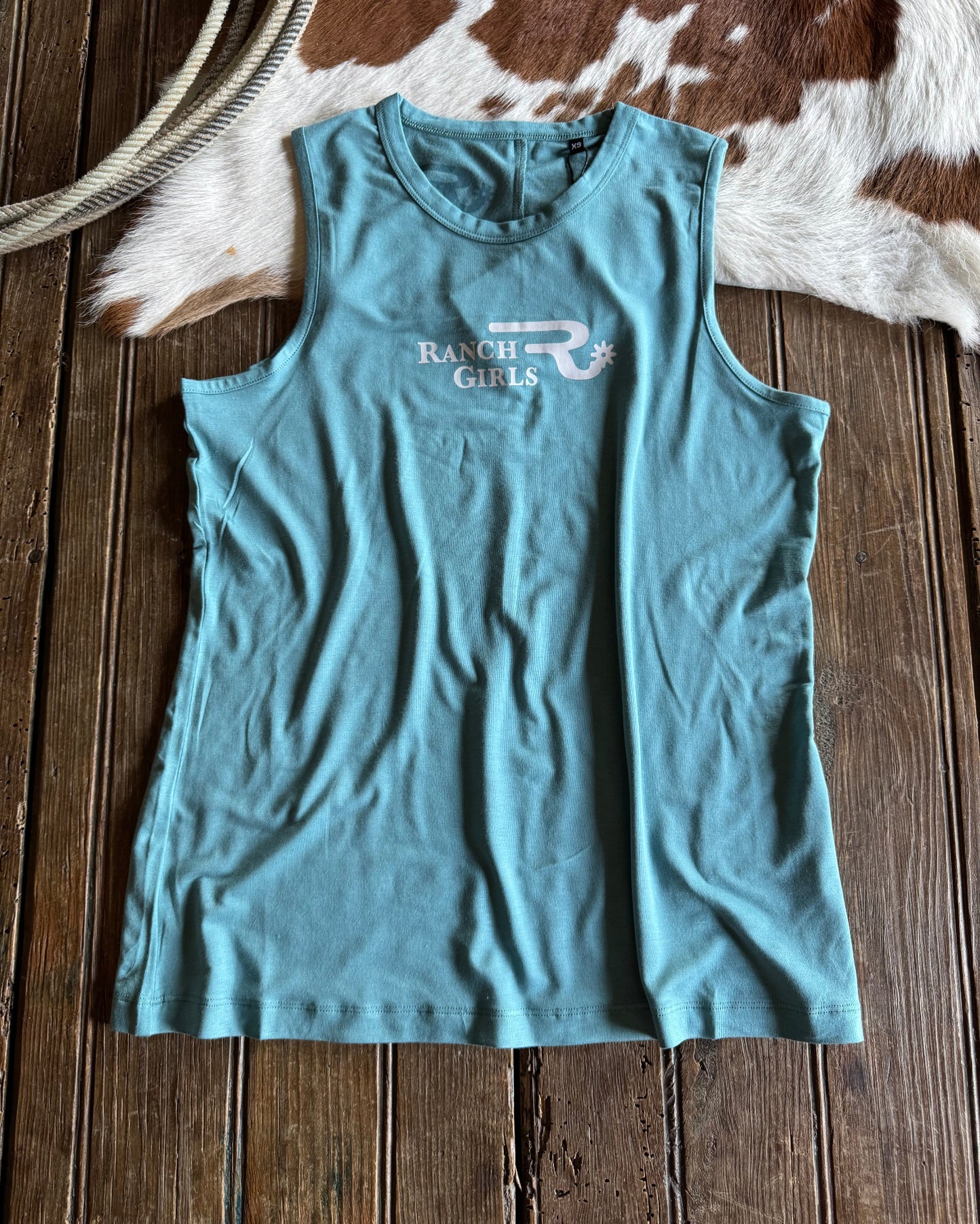 Blue tank top with a logo on a wooden surface next to a cowhide rug