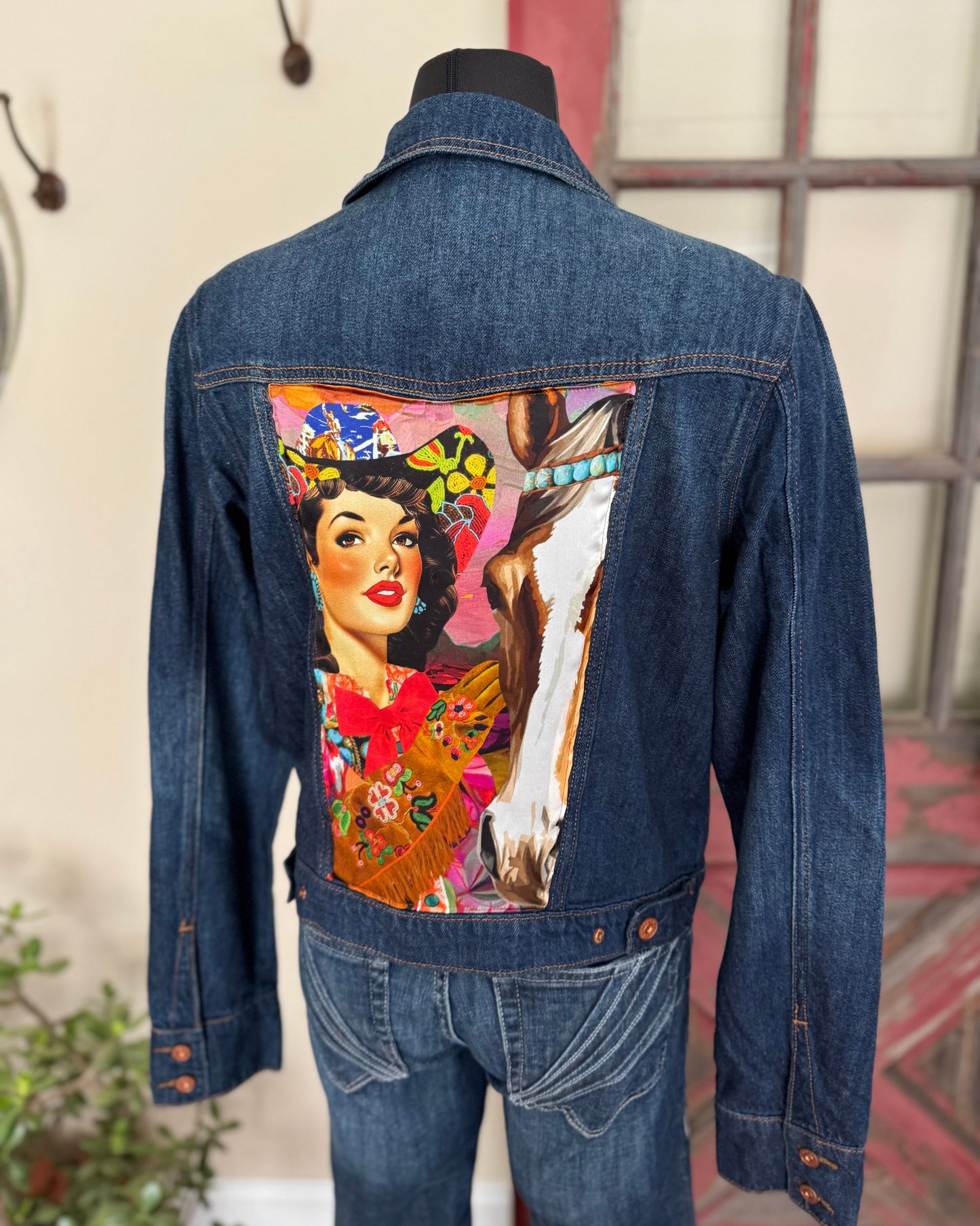 Denim jacket with a colorful graphic of a woman and deer on the back, displayed on a mannequin.