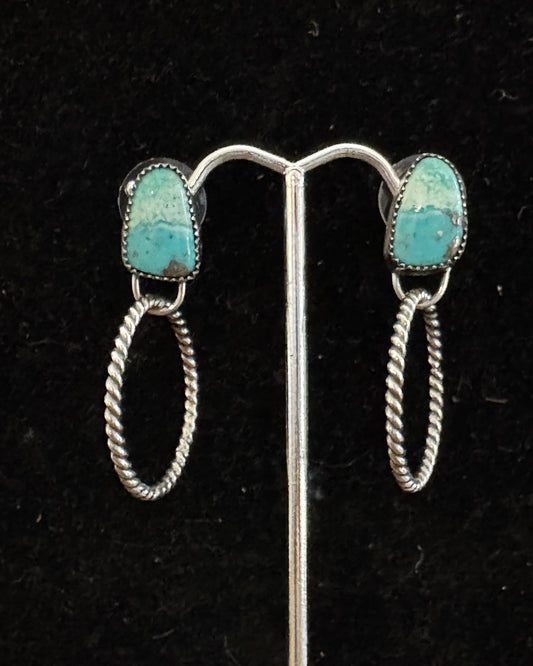 Pair of silver earrings with turquoise stones on a black background