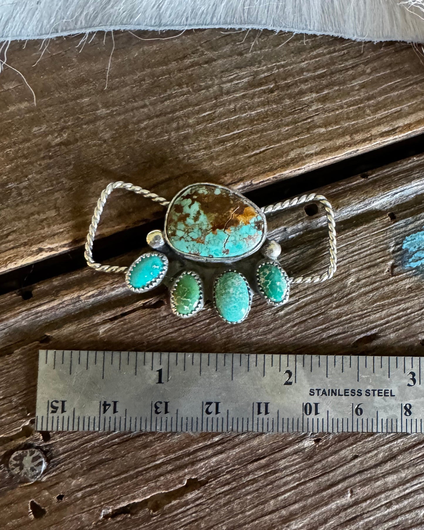 Turquoise and silver twilly slide on a wooden surface with a ruler for scale.